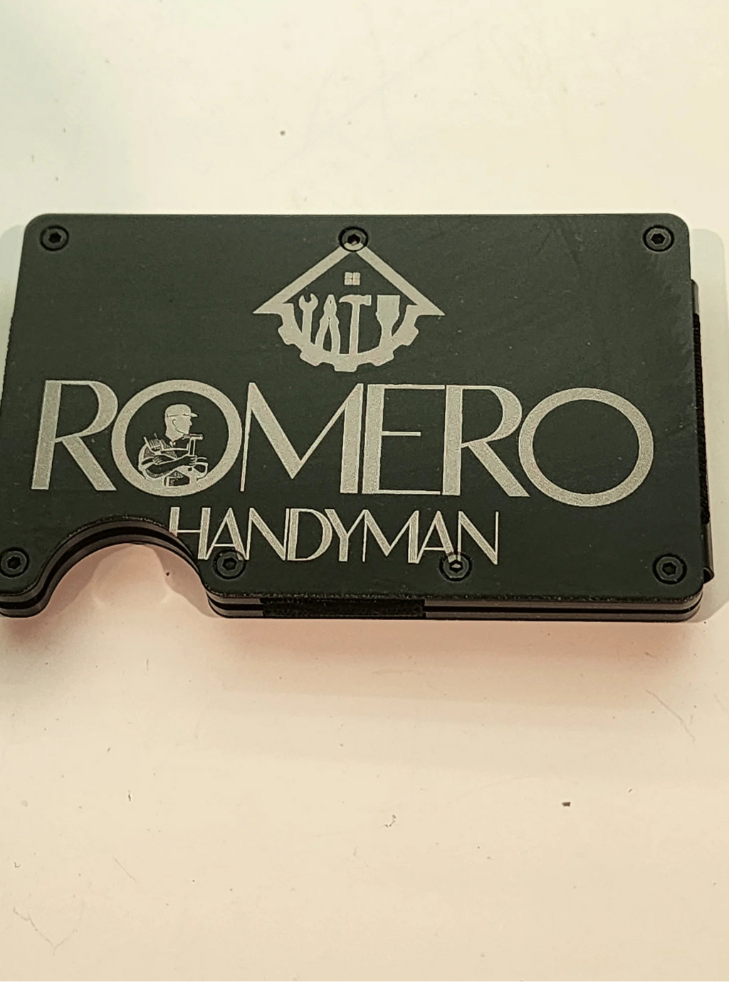 Black cardholder with 'Romero Handyman' text and logo on a beige background
