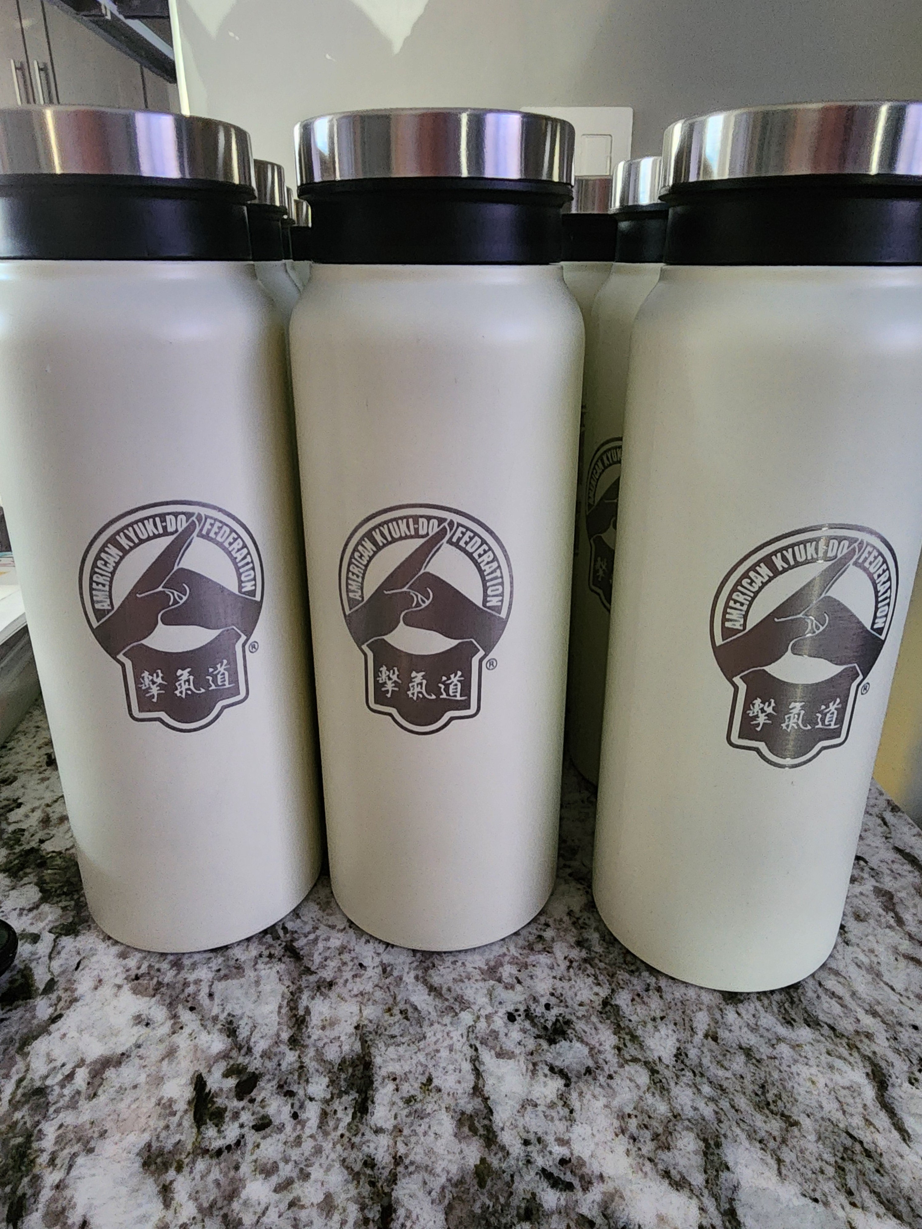 Three white tumblers with a logo on a marble surface