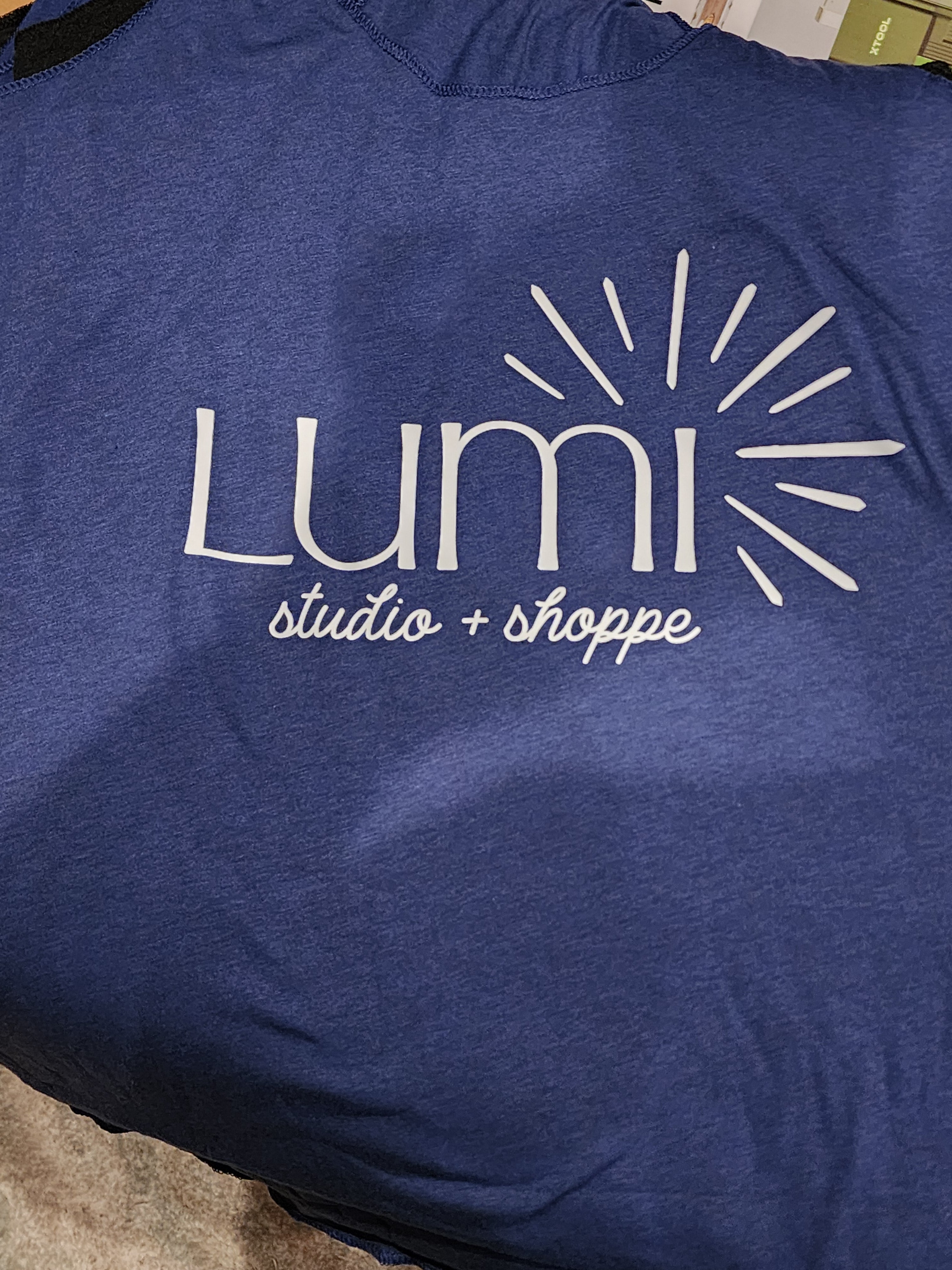 Blue shirt with 'Lumi Studios + Shoppe' logo on a blue background