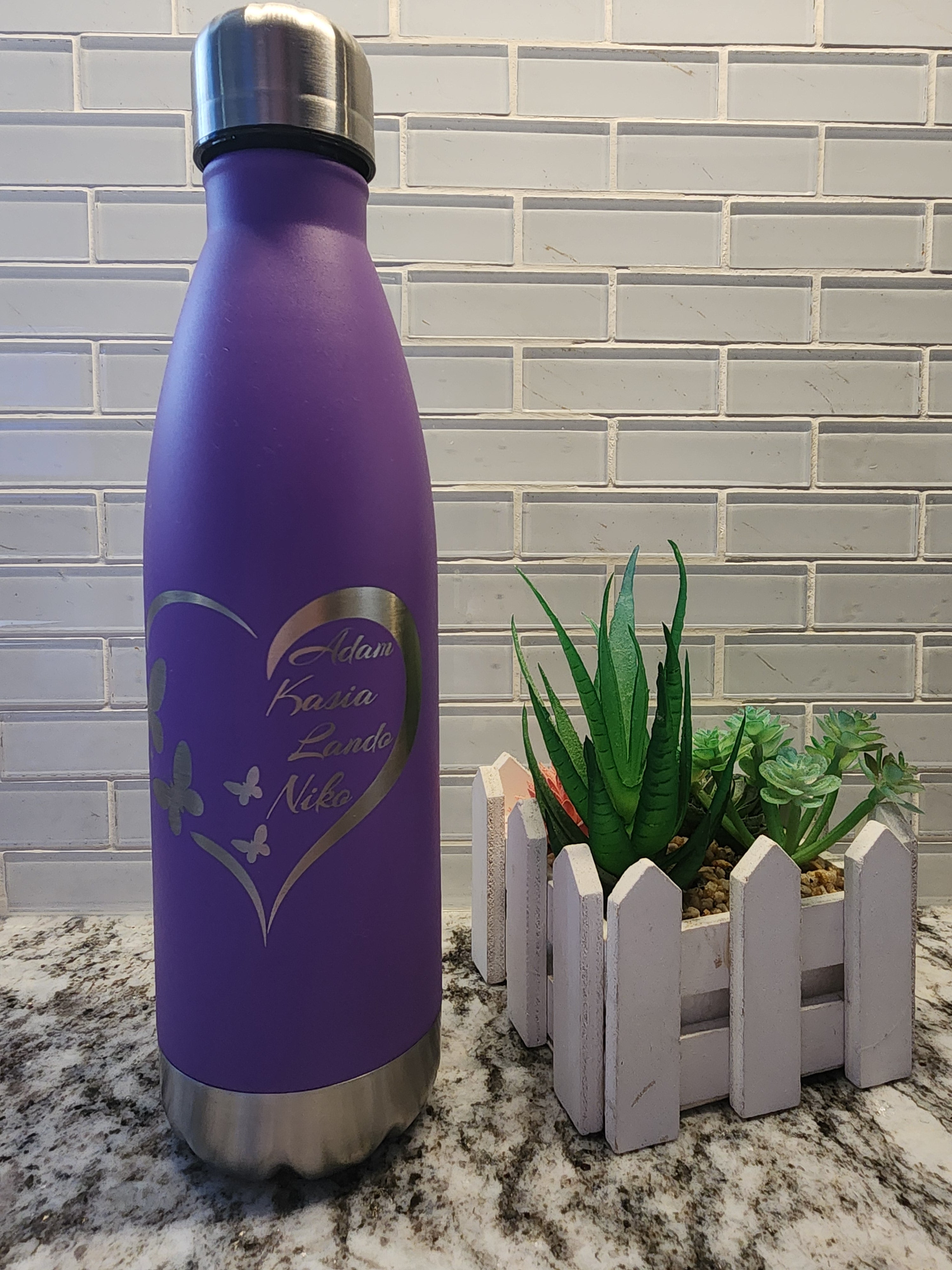 Purple water bottle with silver cap on a tiled floor with a plant in the background