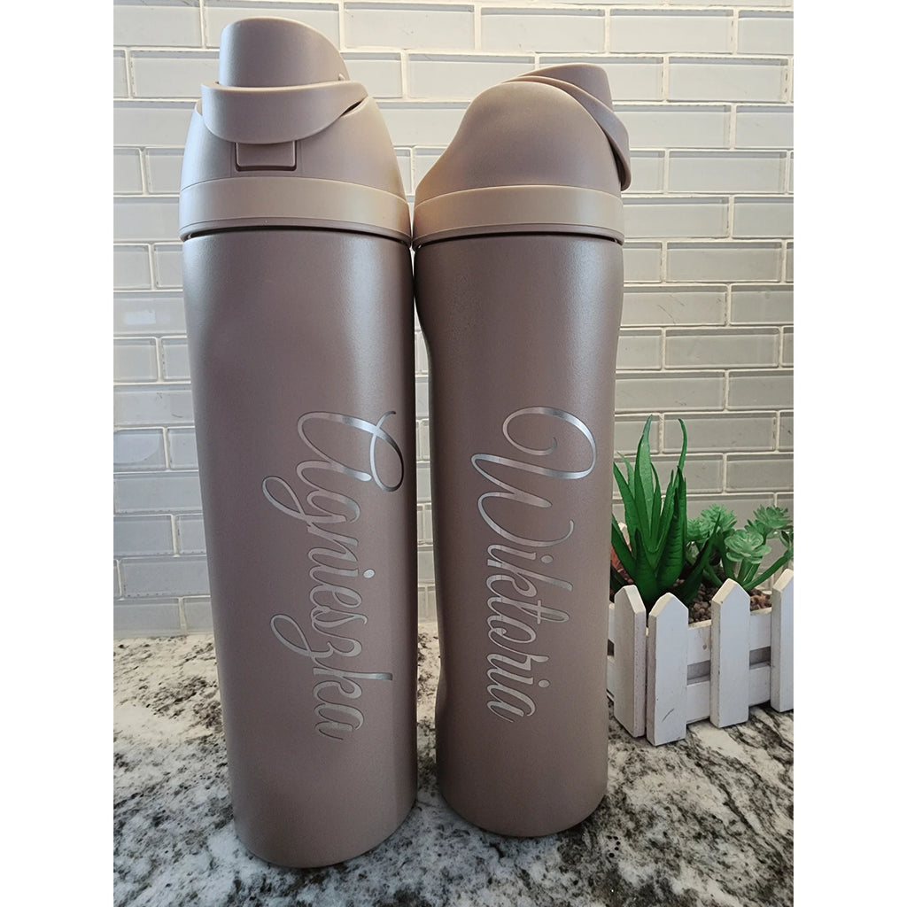Two gray water bottles with engraved names on a marble surface.