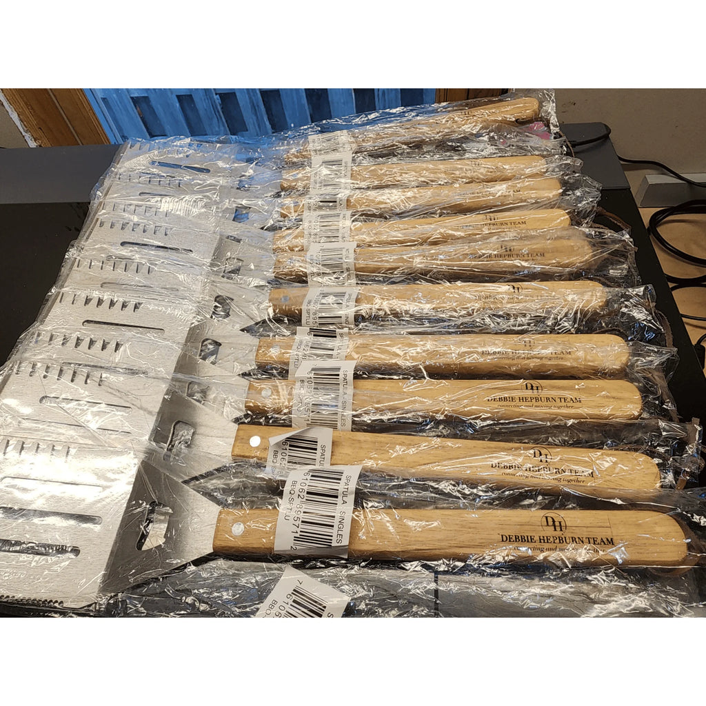 Set of spatulas with wooden handles and metal blades, wrapped in plastic, on a table.