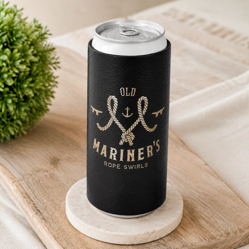A black can cooler sleeve with a gold nautical design reading 'OLD MARINER'S ROPE SWIRLS' and 'CAN NEVER BE TOO MARINER', shown holding a silver can on a round coaster in a styled tabletop setting.