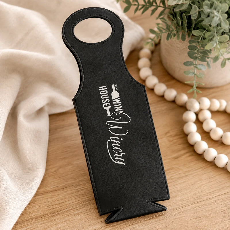 A black faux-leather wine bottle opener with white printed text reading 'WINE HOUSE Nicely' and a wine bottle icon, displayed on a wooden tabletop with a cream fabric drape, wooden beads, and a potted plant.