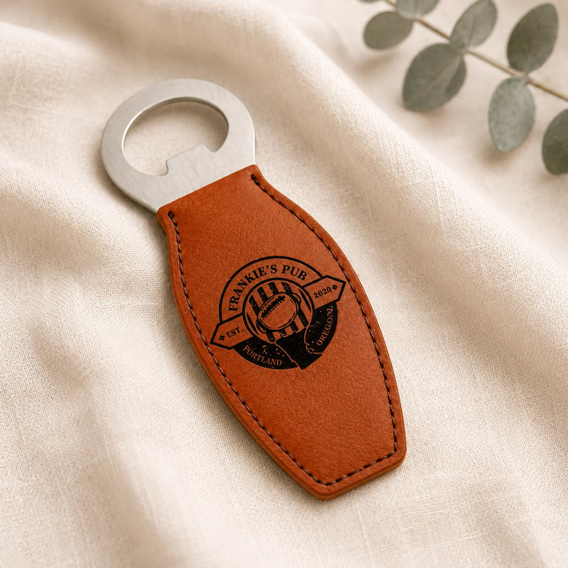 A brown leather bottle opener keychain with a silver metal opener blade, featuring an embossed circular 'Frankie's Pub Portland' logo, displayed on a textured cream fabric background with a green leaf sprig.