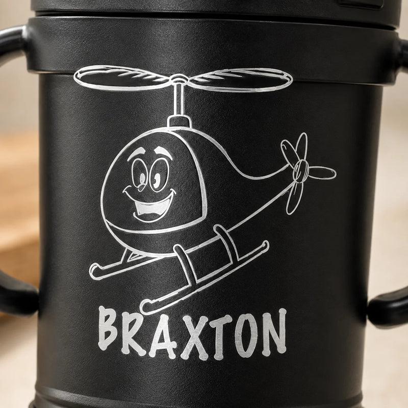 A close-up of a black insulated tumbler with a cartoon helicopter graphic and the name 'BRAXTON' printed in white on the front.