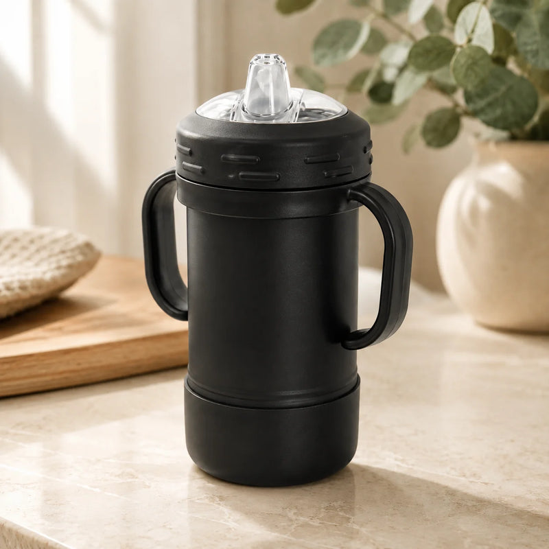 A matte black insulated travel tumbler with two side handles, a clear lid, and a transparent straw, set on a light beige marble countertop with a blurred kitchen background.