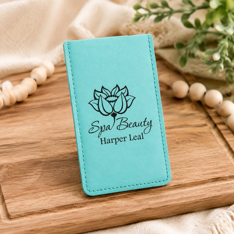 A turquoise blue faux-leather card holder or wallet with black printed text reading 'Spa Beauty Harper Leaf' and a lotus flower graphic, displayed on a wooden board with neutral fabric and beads in the background.