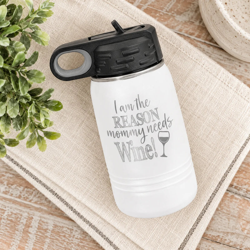 A white insulated water bottle with a black lid, placed on a beige woven placemat over a wooden surface. The bottle has gray text that reads 'I am the REASON mommy needs Wine!' with a wine glass icon.